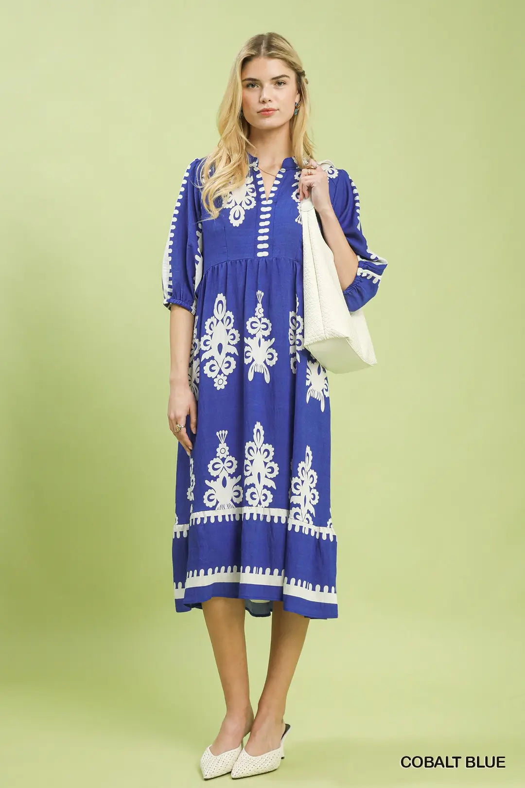 Woman wearing a cobalt blue dress with white patterns on a light green background