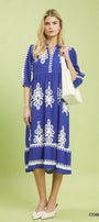 Woman wearing a cobalt blue dress with white patterns on a light green background