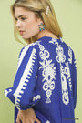 Woman wearing a blue dress with white embroidery against a light green background
