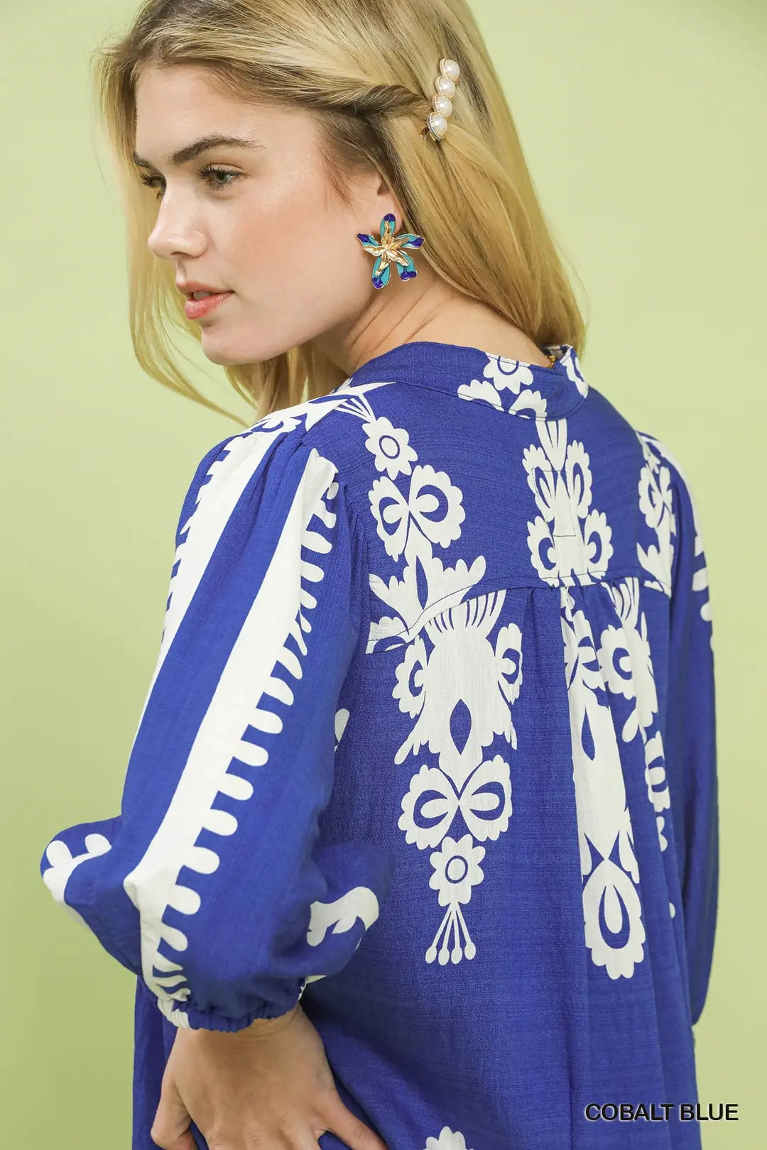 Woman wearing a blue dress with white embroidery against a light green background