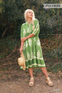 Woman wearing a green dress with white patterns standing outdoors.