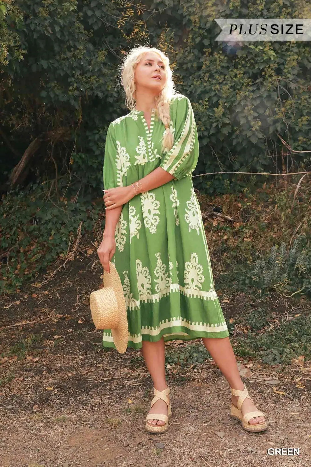 Woman wearing a green dress with white patterns standing outdoors.