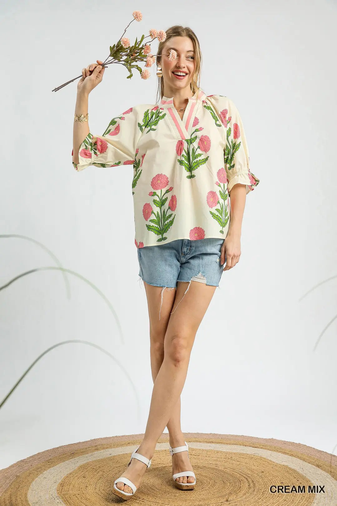Woman wearing a floral blouse and denim shorts holding flowers on a white background