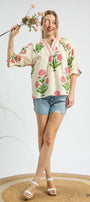 Woman wearing a floral blouse and denim shorts holding flowers on a white background