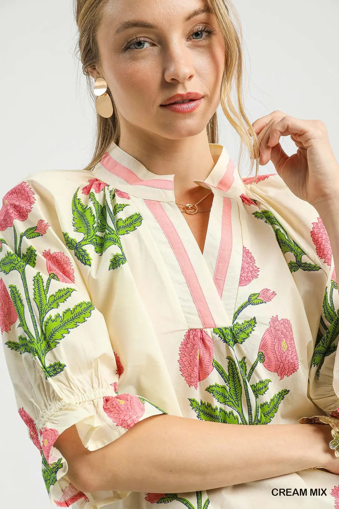 Woman wearing a cream blouse with pink floral embroidery on a white background