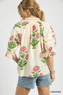 Woman wearing a cream blouse with floral patterns and denim shorts on a white background