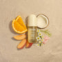 Kit-sch Coastal Sorbet perfume bottle surrounded by fruit slices and flowers on a beige background