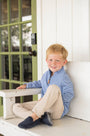 Young boy sitting on a step in front of a white door with green window frames.