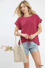 Woman holding a woven bag and wearing a berry-colored top and denim shorts on a white background