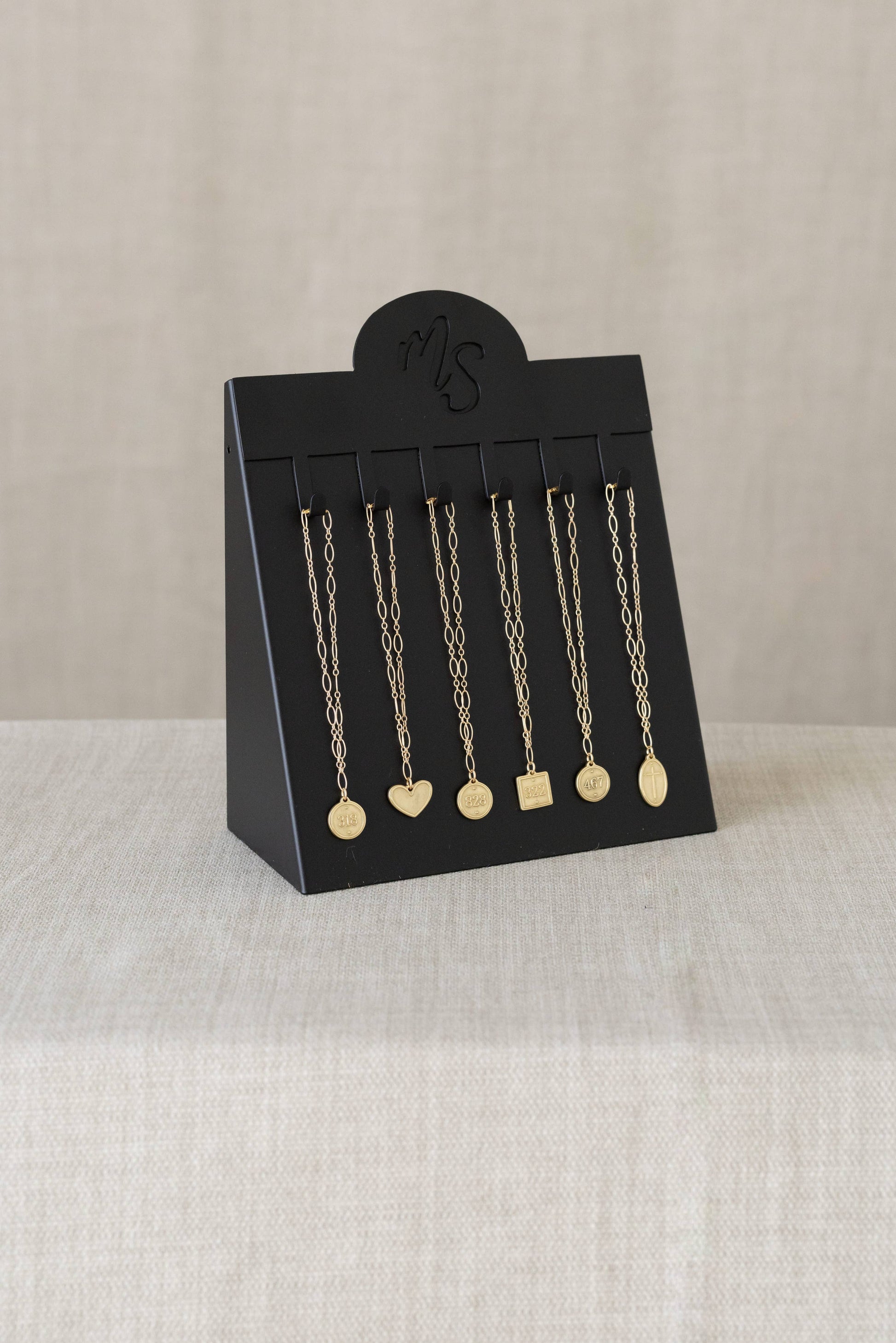 Black jewelry display card with gold necklaces on a beige background