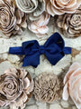 Navy blue bow headband surrounded by beige and pink floral arrangements on a textured surface.