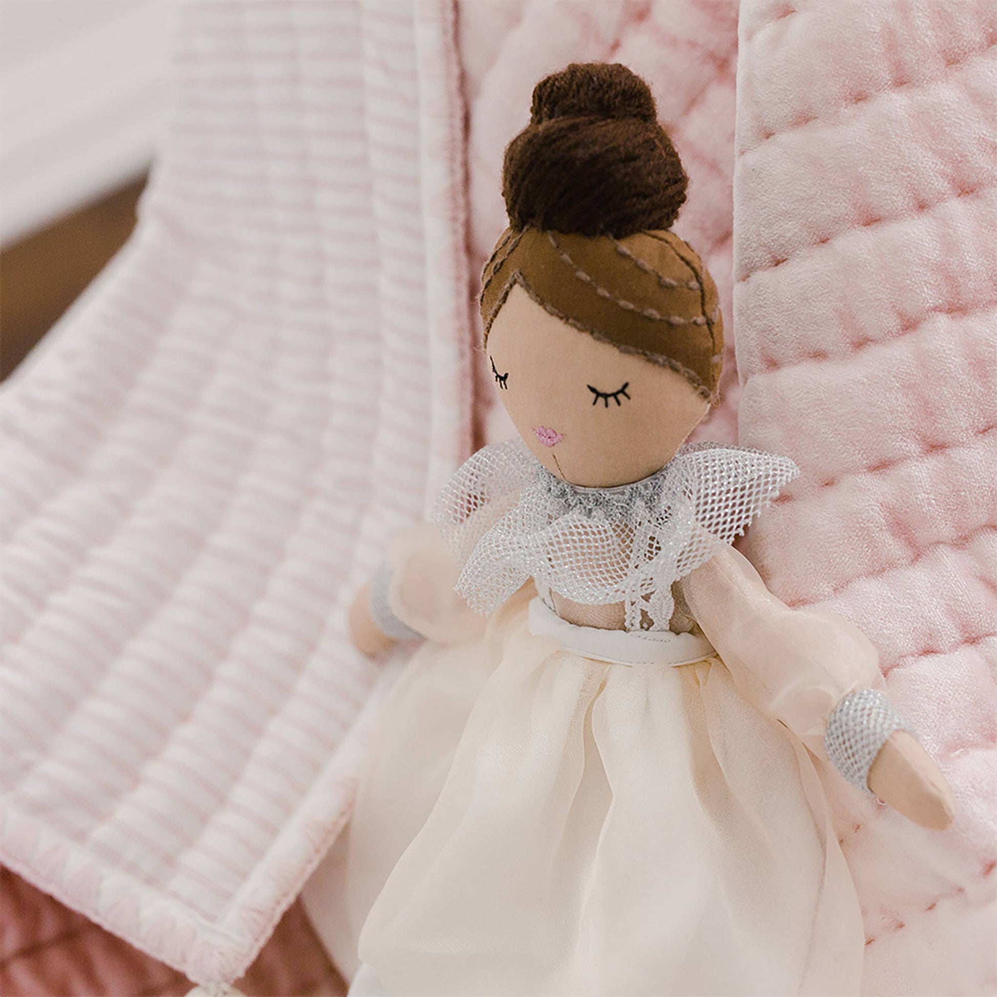 Textile doll with brown hair and a white dress on a pink textured background