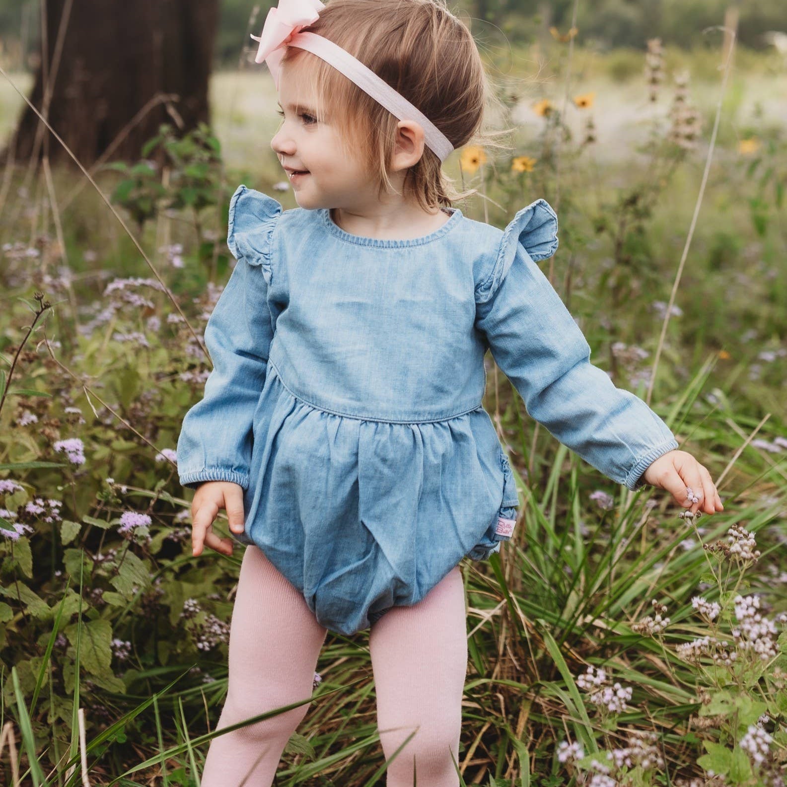 Child in a blue romper standing in a field with flowers