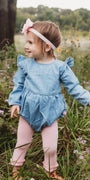 Child in a blue romper standing in a field with flowers