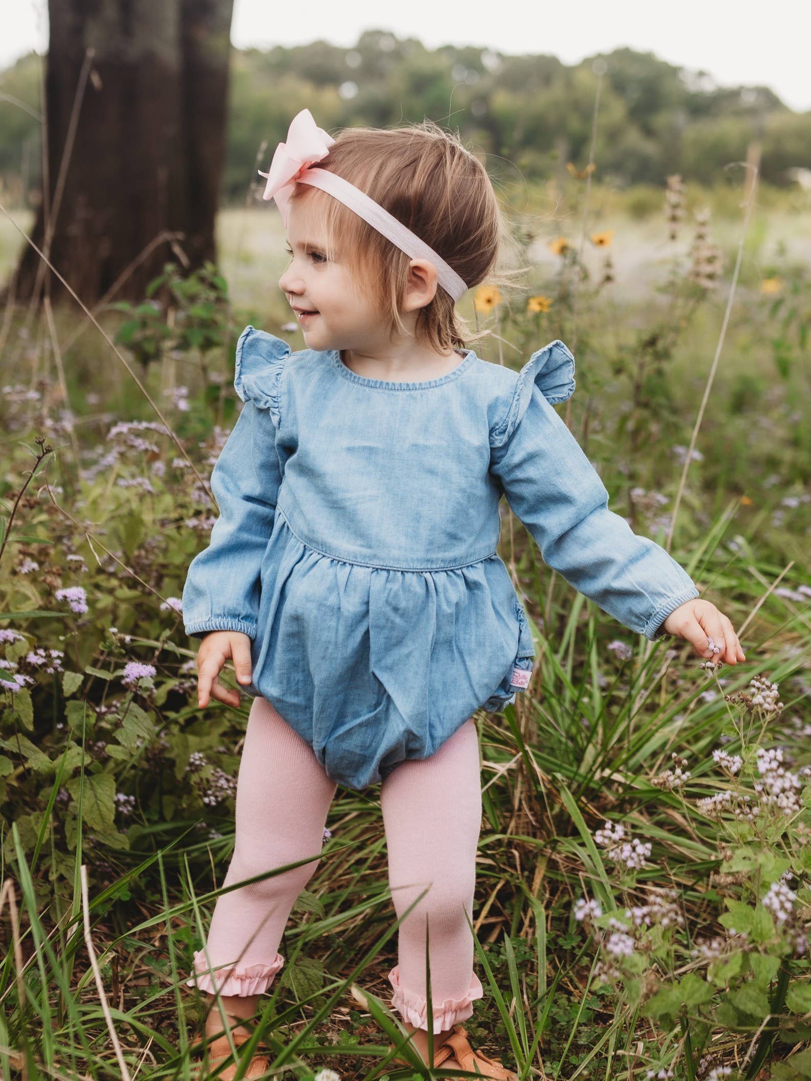 Child in a blue romper standing in a field with flowers