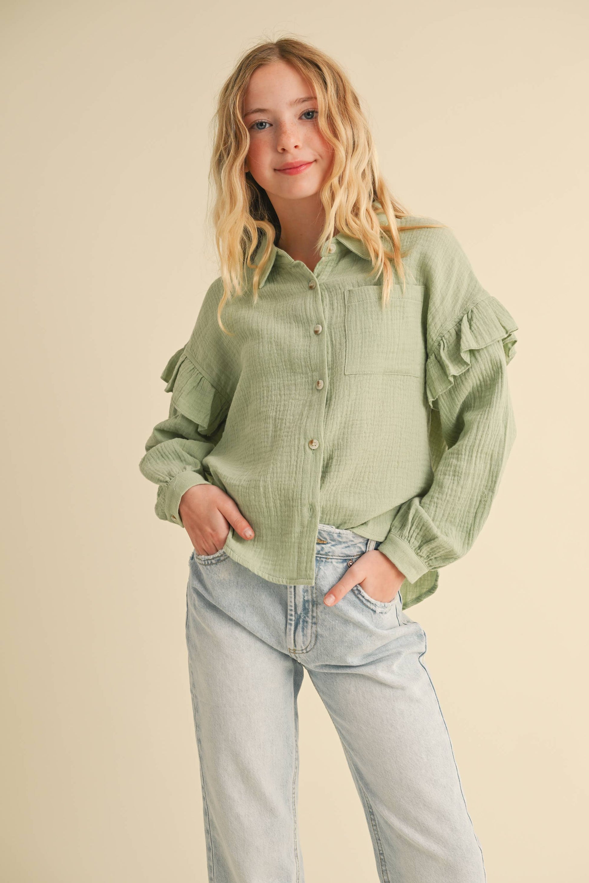 Person wearing a green button-up shirt and light blue jeans on a beige background