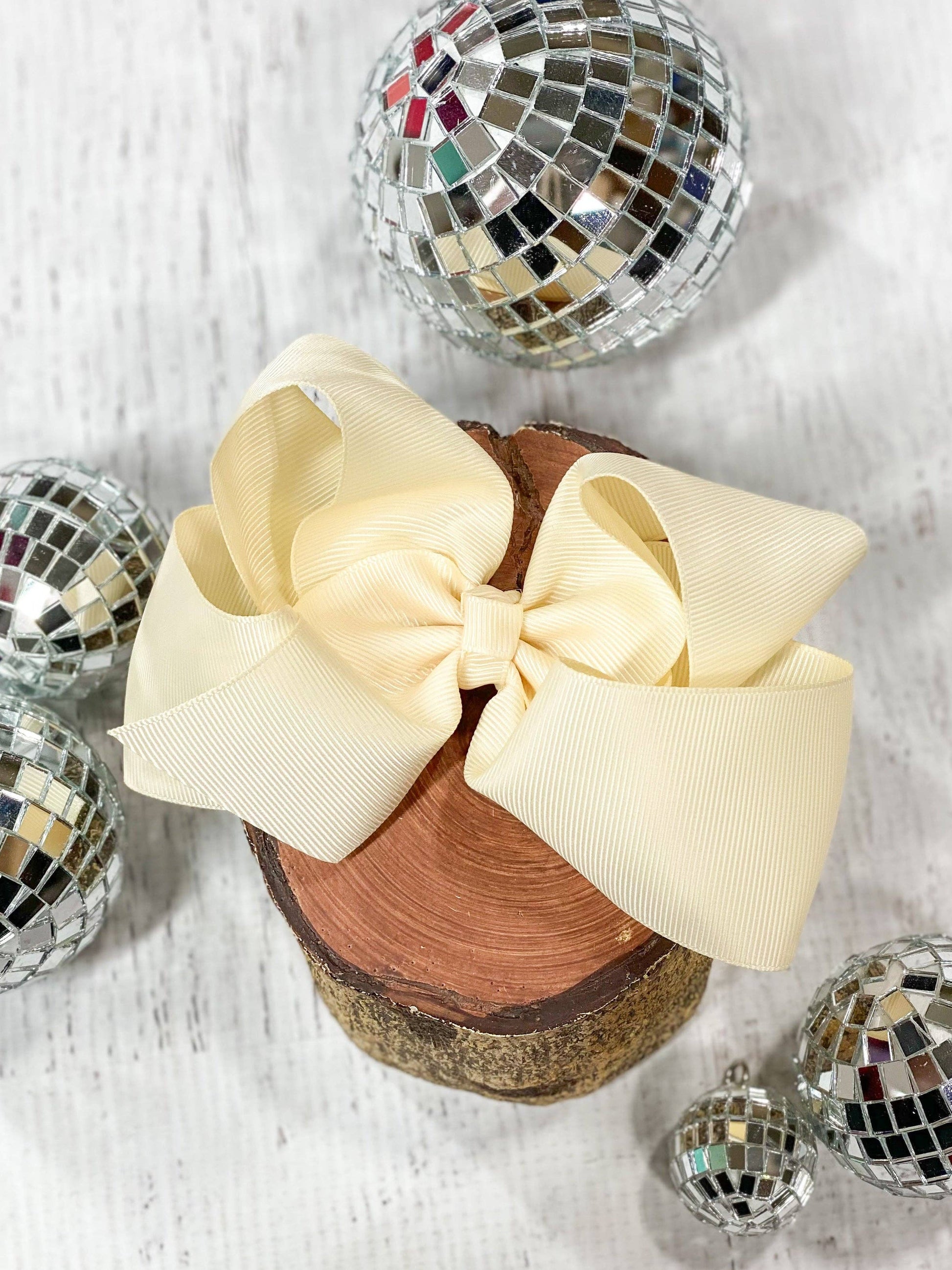 Wooden block with a large beige bow, surrounded by disco balls on a light background