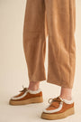 Brown platform shoes with white laces worn with beige pants on a neutral background