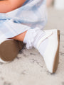 White shoes with brown soles worn by a person sitting on a marble surface.