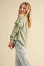Young girl wearing a green blouse and light blue jeans against a beige background