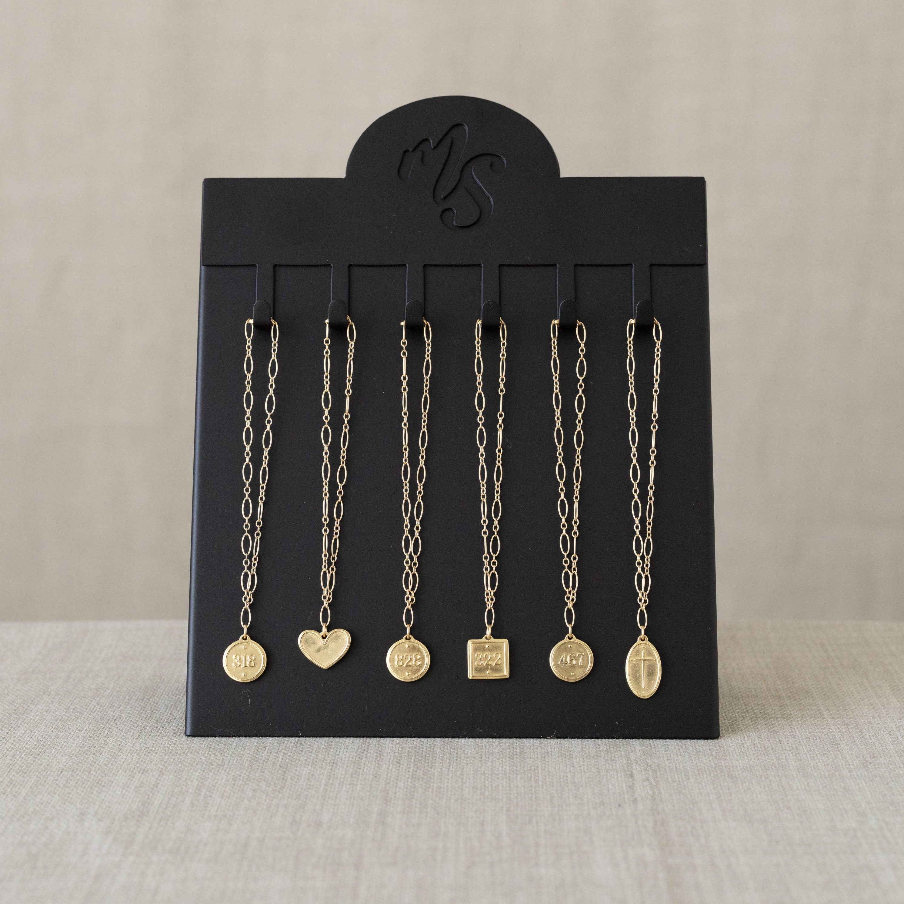 Black jewelry display card with hanging necklaces on a beige background