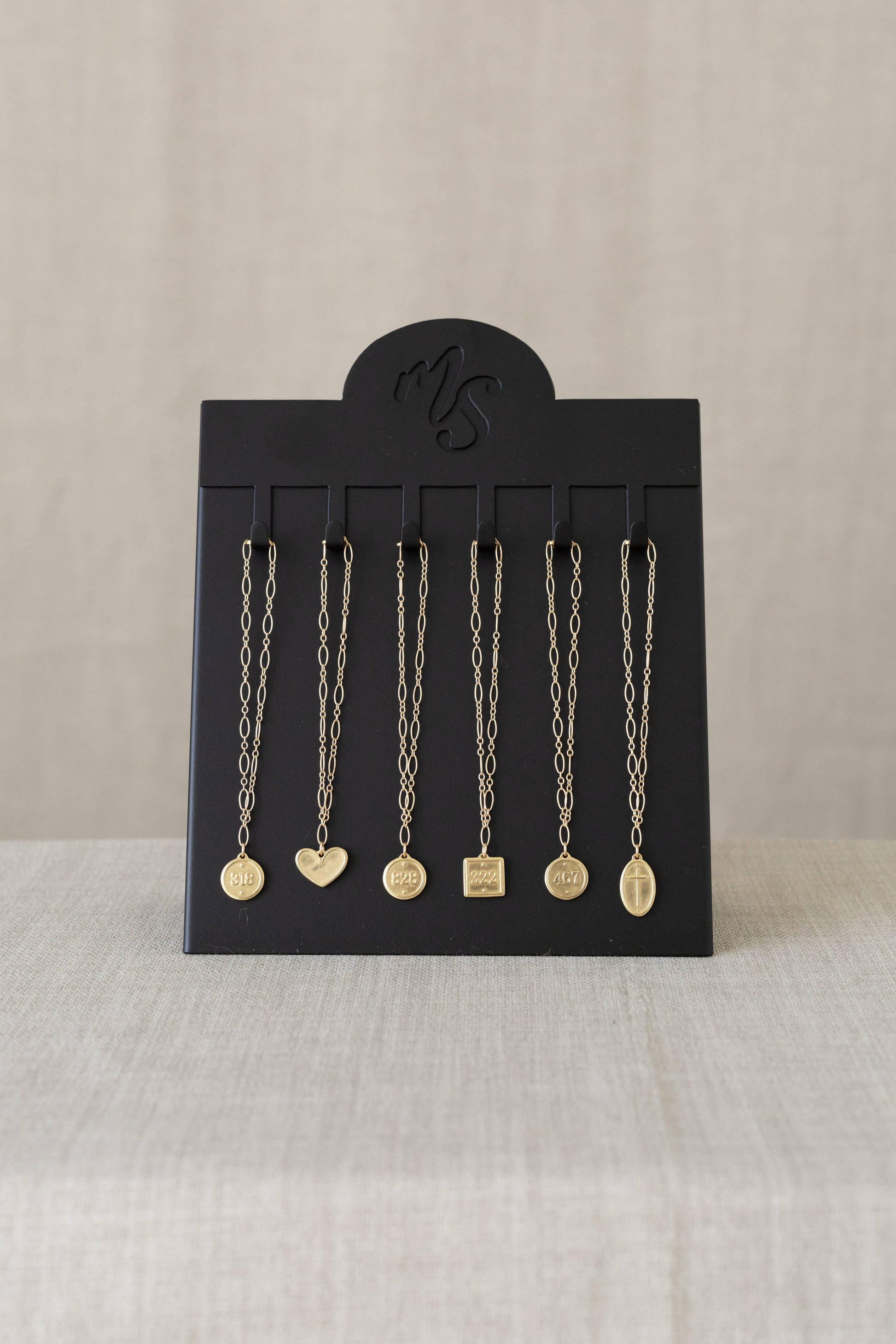 Black jewelry display card with hanging necklaces on a beige background