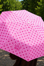 Pink polka dot umbrella with 'LULU MAC' branding held by a person outdoors.