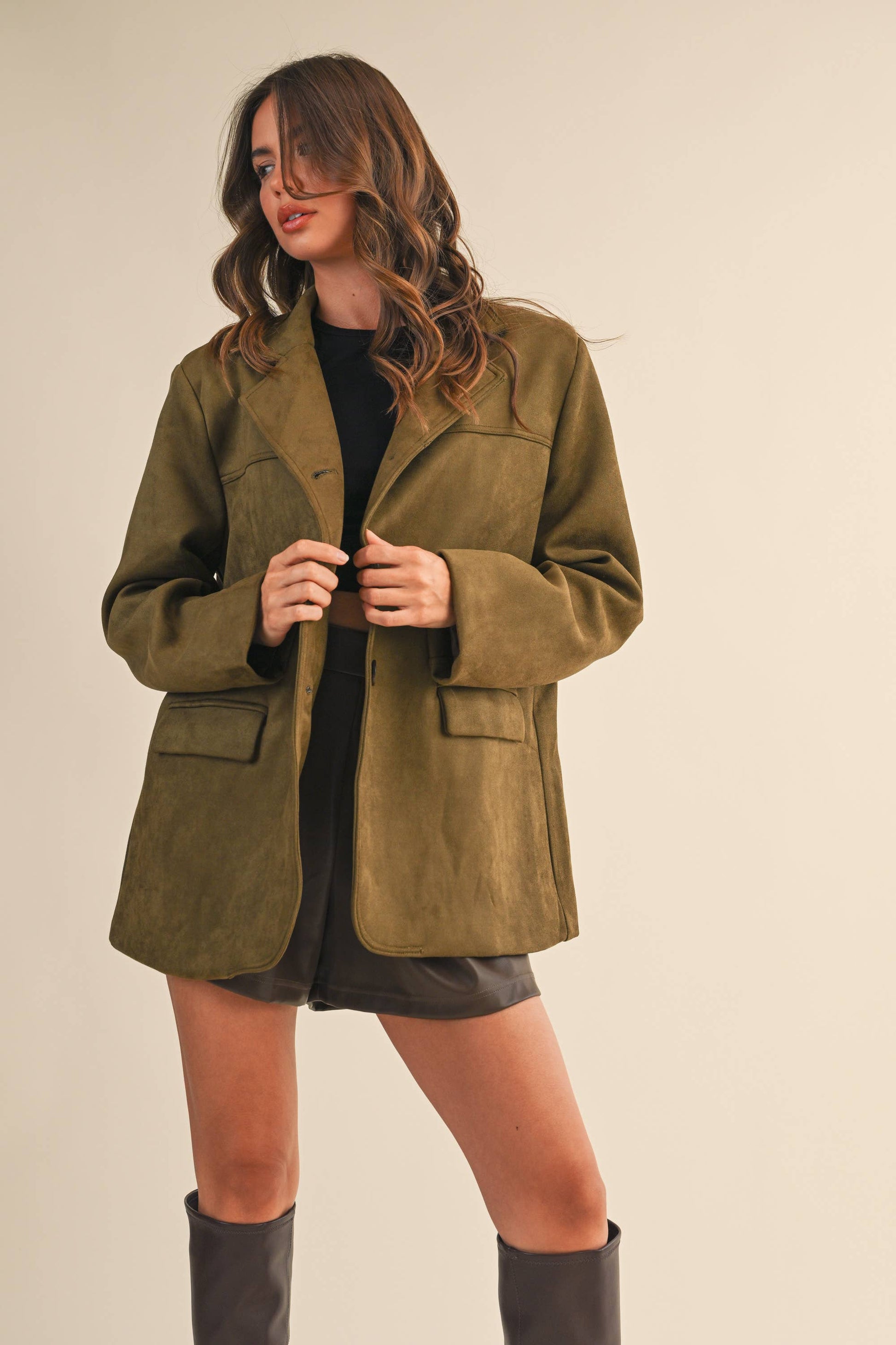 Woman wearing an olive green suede jacket on a beige background