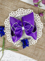 Purple hair bow on a white doily with flowers on a textured surface