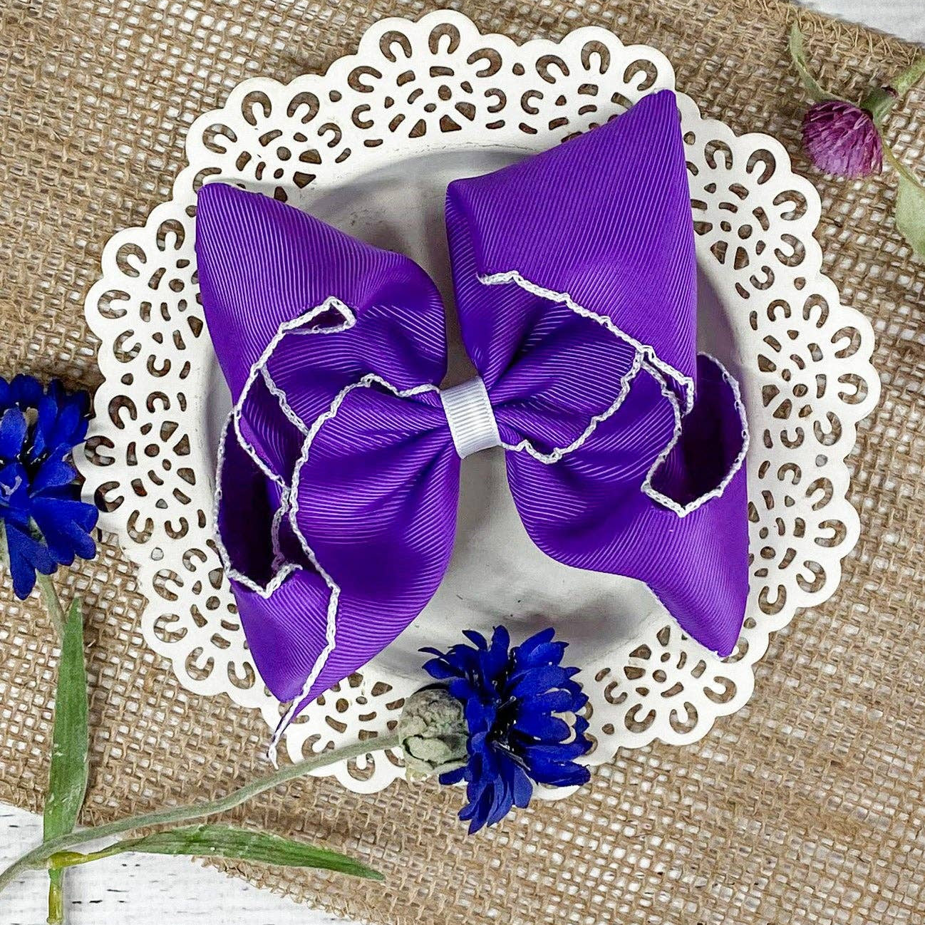 Purple hair bow on a white doily with flowers on a textured surface