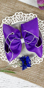 Purple hair bow on a white doily with flowers on a textured surface