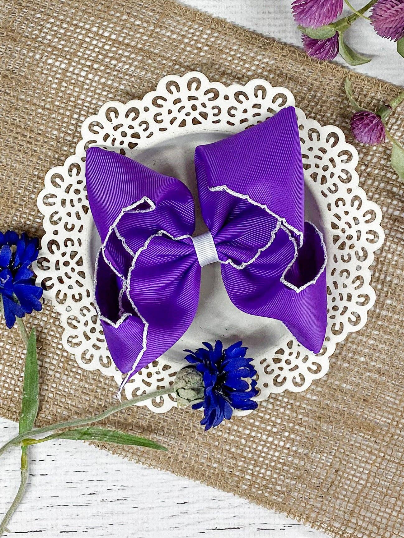 Purple hair bow on a white doily with flowers on a textured surface