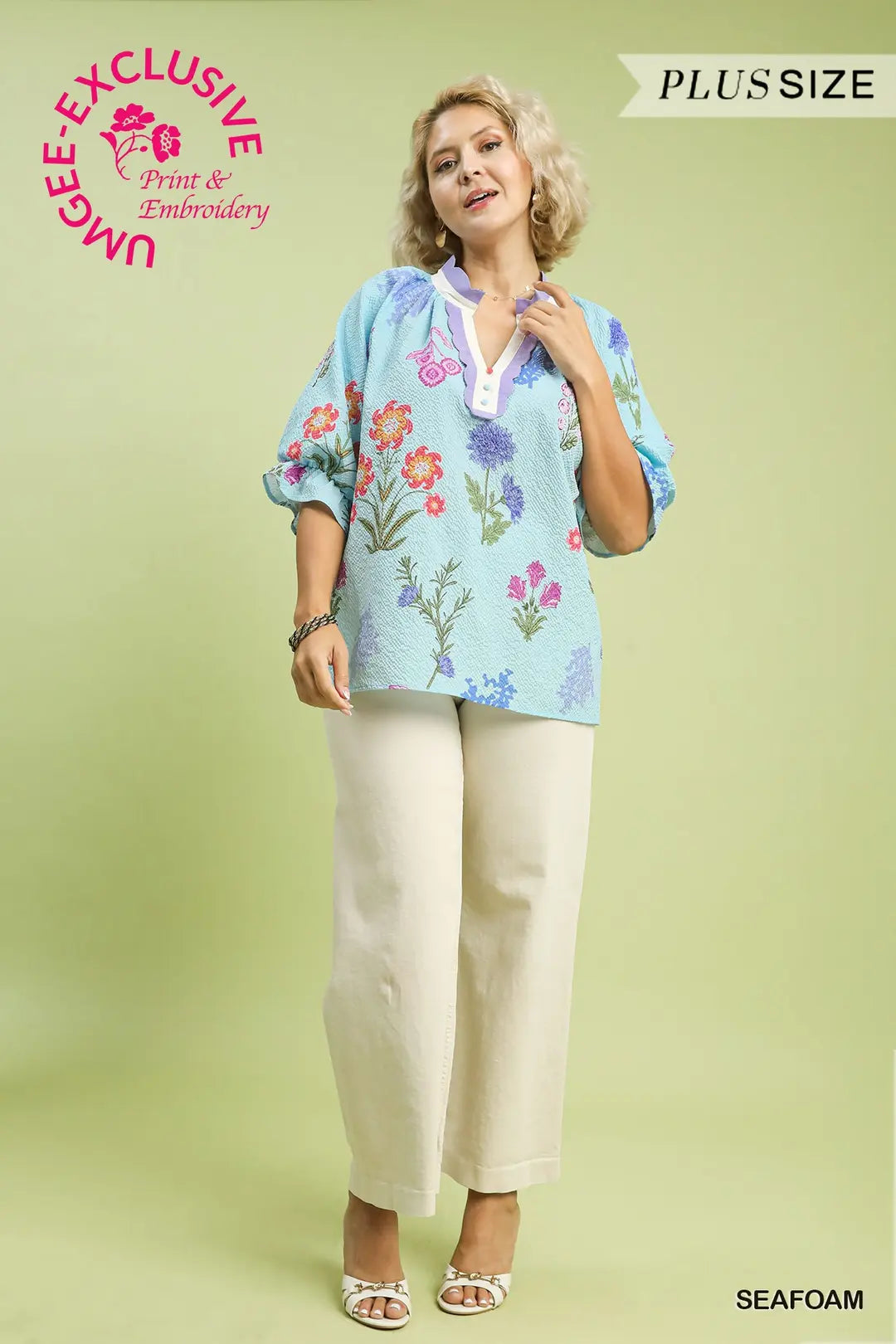 Woman wearing a floral blouse and beige pants on a light green background with 'UMgee Exclusive' branding.