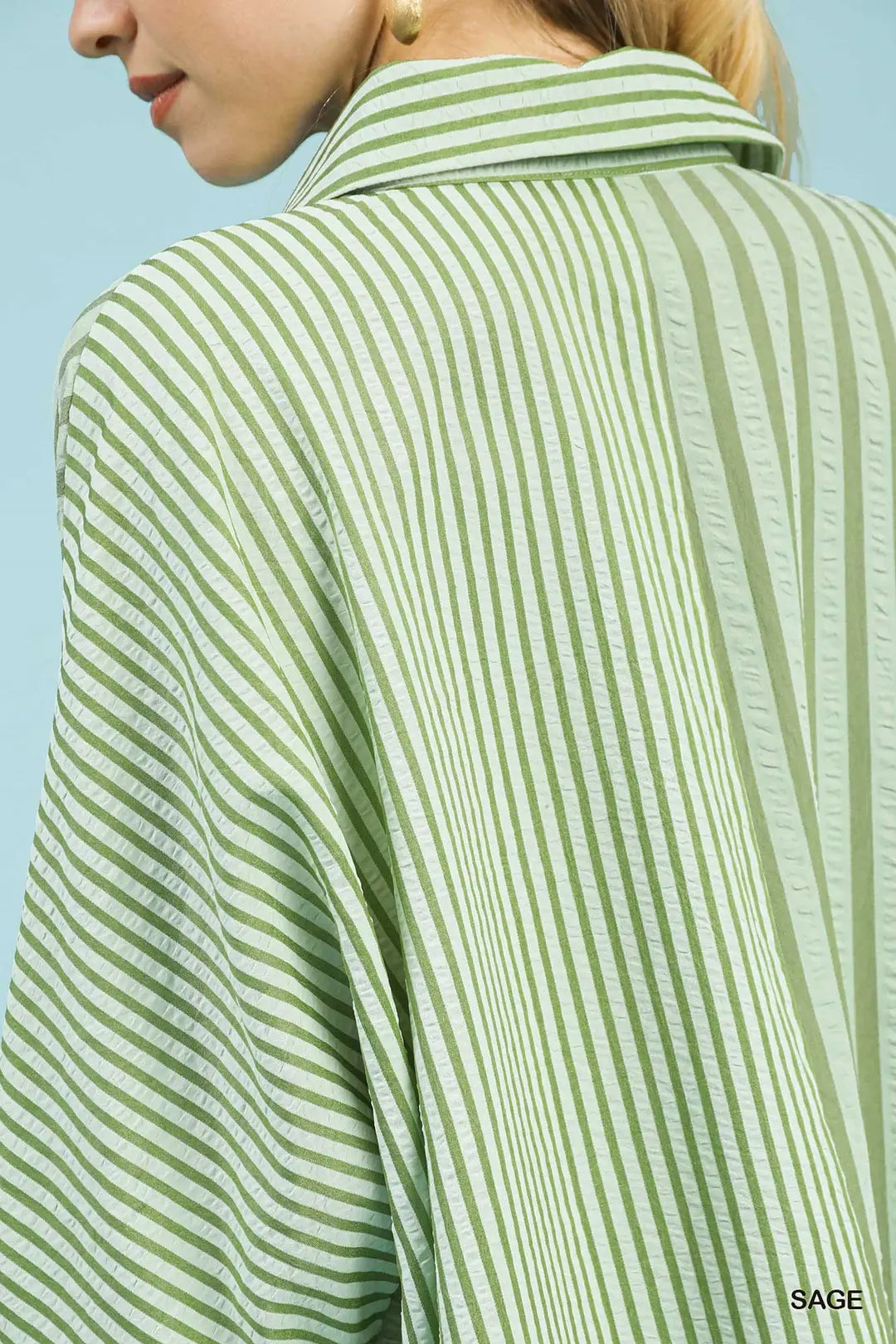 Green and white striped shirt worn by a person against a light blue background