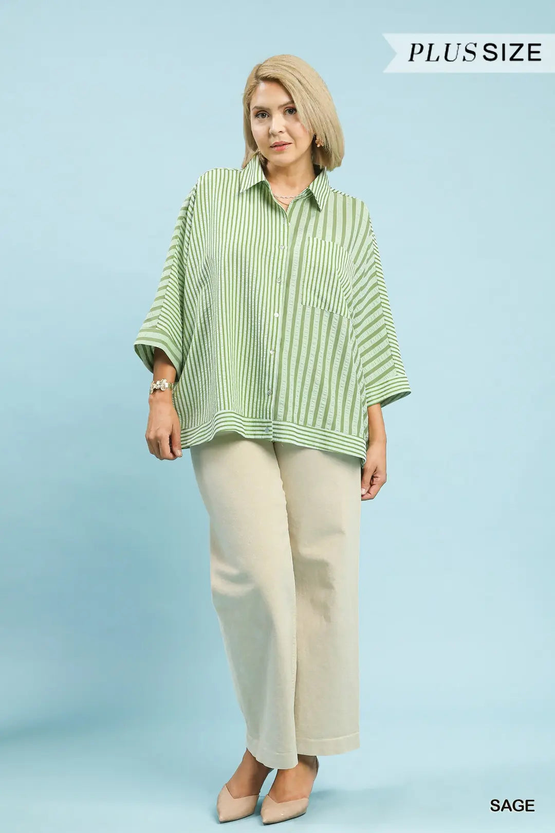 Woman wearing a green striped shirt and beige pants on a light blue background