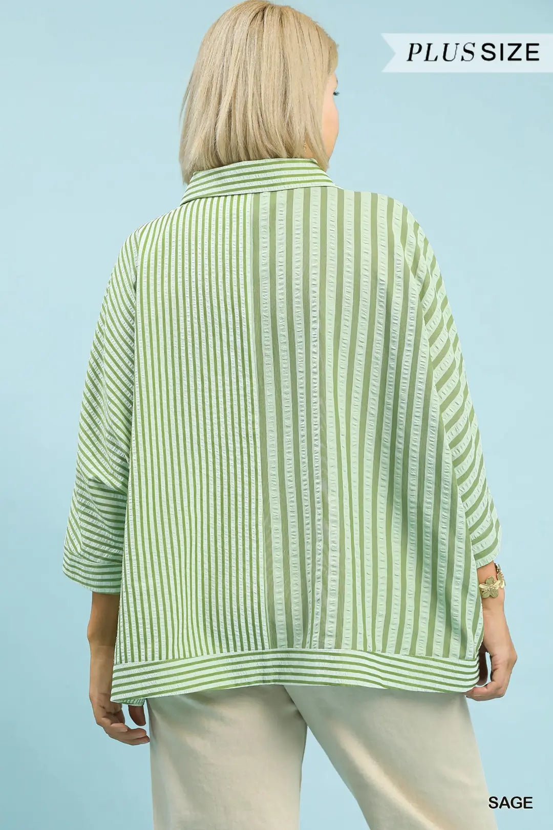 Woman wearing a green and white striped plus-size shirt against a light blue background.
