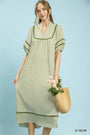 Woman wearing a light olive striped dress holding a straw bag with flowers on a light blue background