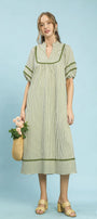 Woman wearing a light olive striped dress holding a woven bag against a light blue background