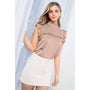 Woman wearing a patterned top and white skirt against a light background