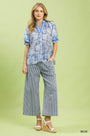 Woman wearing a blue patterned top and striped pants on a light green background