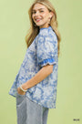 Woman wearing a blue floral blouse with ruffled sleeves on a light green background
