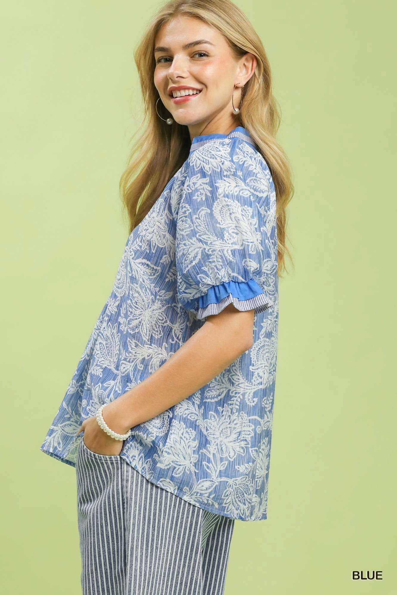 Woman wearing a blue floral blouse with ruffled sleeves on a light green background