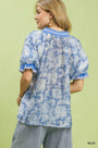 Woman wearing a blue and white patterned blouse with ruffled sleeves against a green background