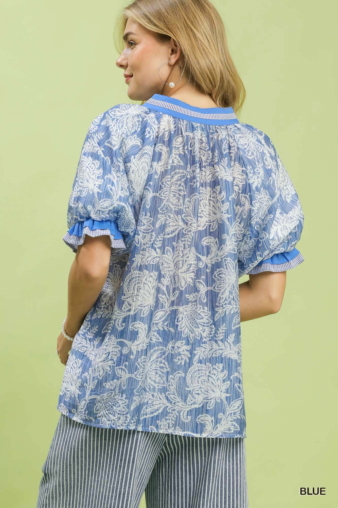 Woman wearing a blue and white patterned blouse with ruffled sleeves against a green background