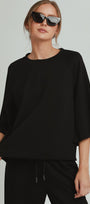 Woman wearing a black outfit with sunglasses on a plain background
