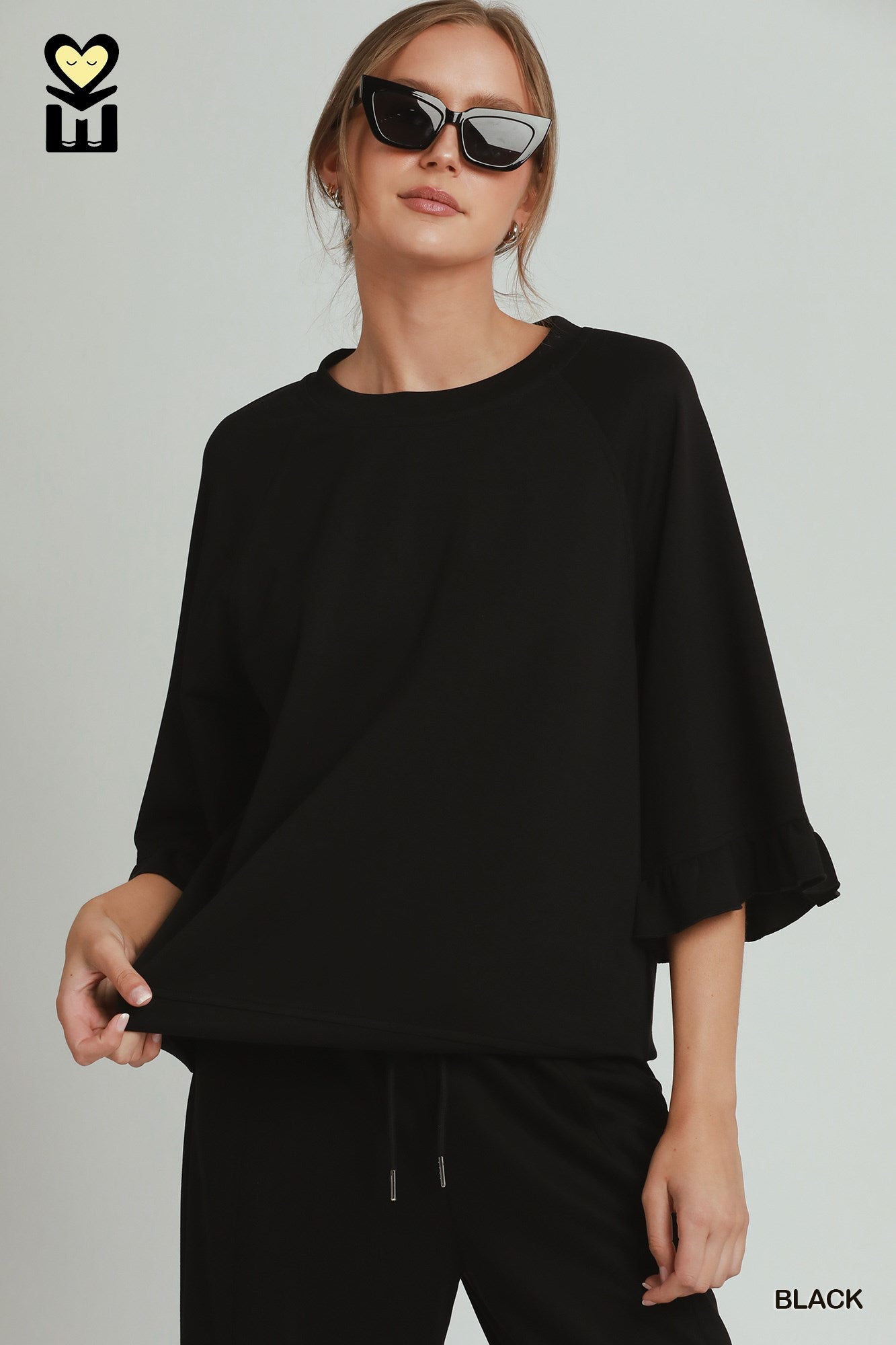 Woman wearing a black outfit with sunglasses on a plain background