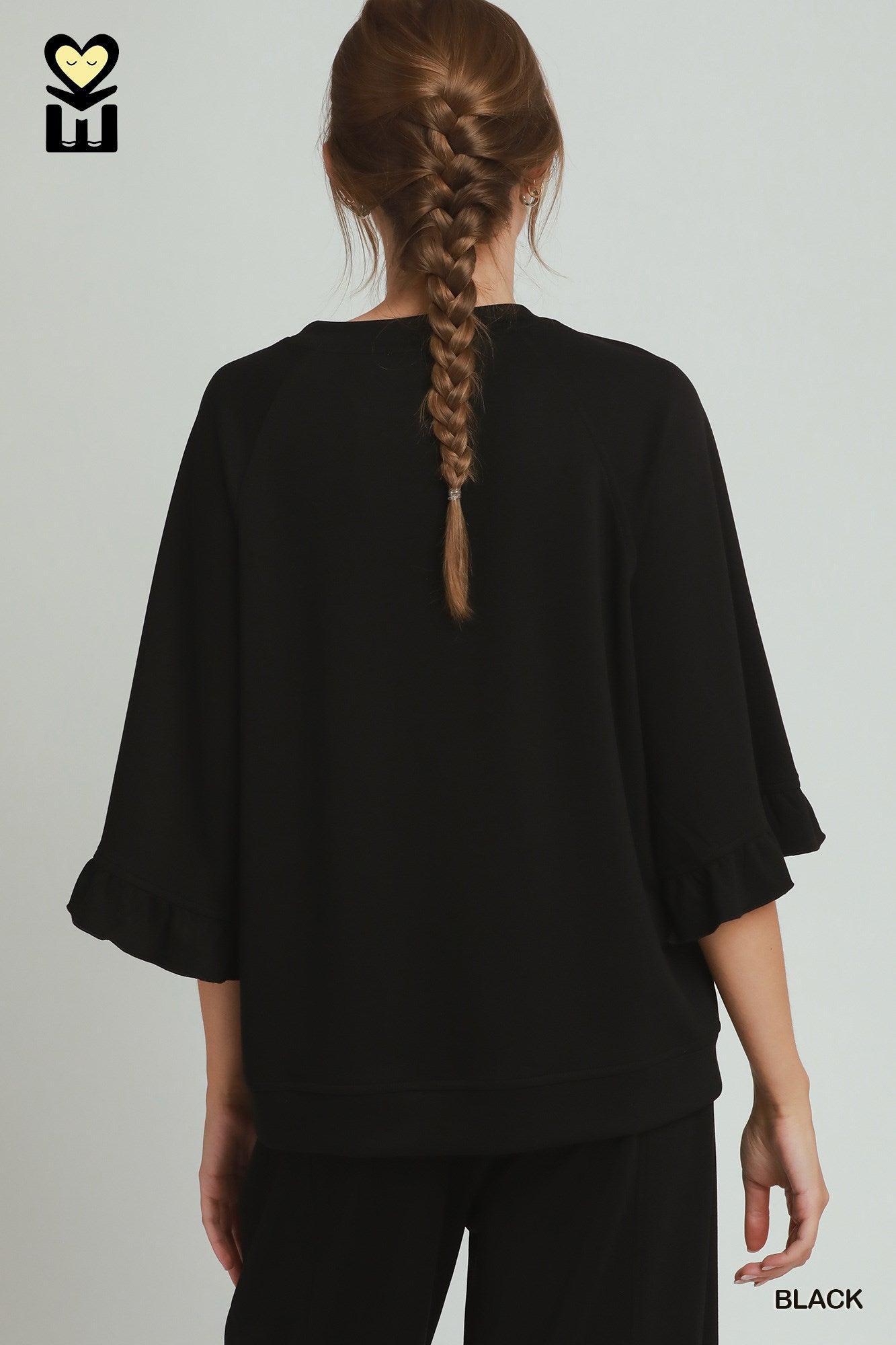 Person wearing a black outfit with a braided hairstyle on a plain background