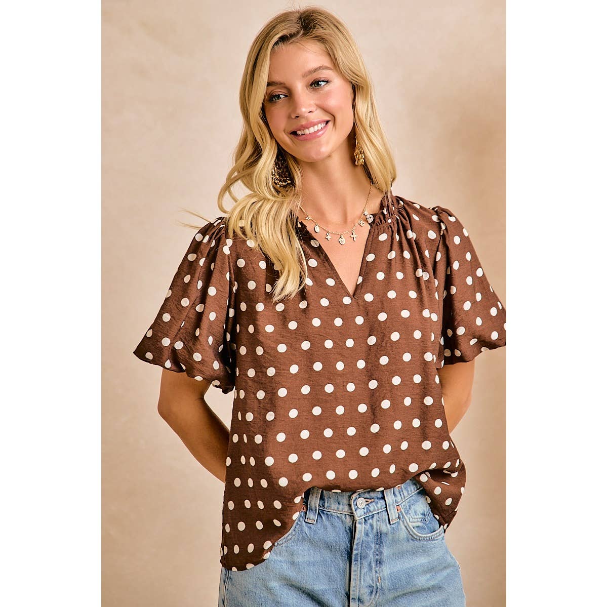 Woman wearing a brown polka dot blouse and blue jeans against a beige background