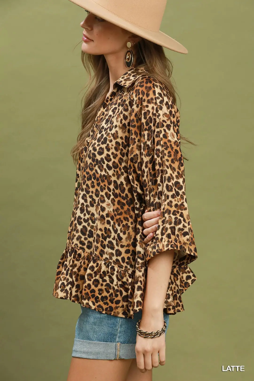 Woman wearing a leopard print blouse and denim shorts against a green background