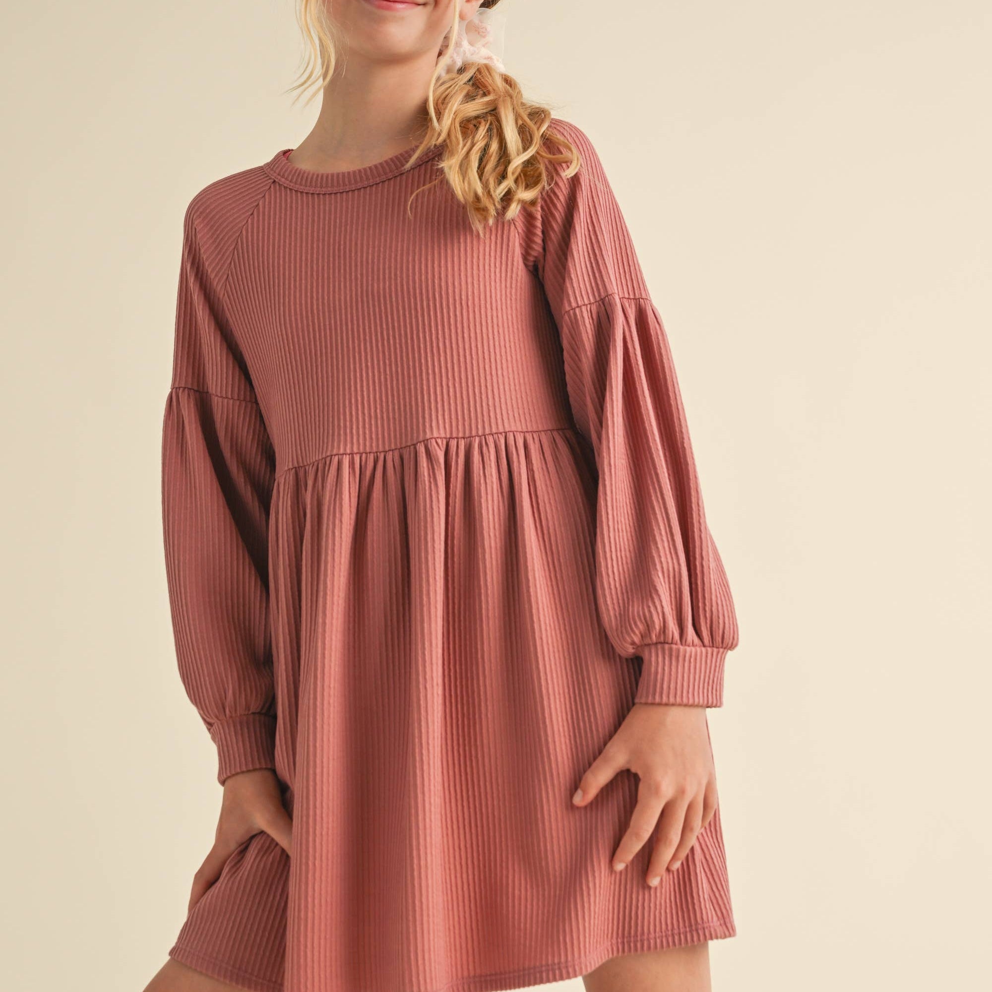 Young girl wearing a ribbed dress with long sleeves on a beige background